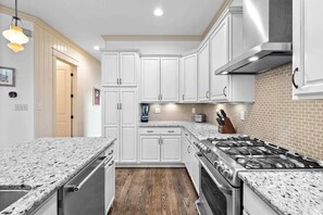 A modern kitchen with white cabinetry, granite countertops, a stainless steel stove, and a wood floor. - Golf Cart+4 Bikes! 5 Min to the Pool, 10 to Beach! 2 King Suites & Custom Bunks! ~ Baha Beach House at WaterSound West on 30A (Santa Rosa Beach)