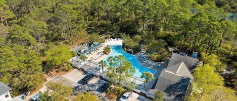 A resort with a swimming pool surrounded by dense trees, a beach in the background, and a clear sky.