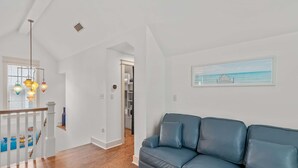 A modern living room with a blue leather sofa, wooden flooring, a staircase with white railings, and a hanging light fixture. - Golf Cart+4 Bikes! 5 Min to the Pool, 10 to Beach! 2 King Suites & Custom Bunks! ~ Baha Beach House at WaterSound West on 30A (Santa Rosa Beach)
