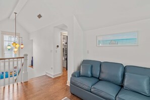 Un salon moderne avec un canapé en cuir bleu, un plancher en bois, un escalier avec des rampes blanches et un luminaire suspendu.