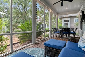 Une terrasse couverte avec de grandes fenêtres, des meubles en osier et une table avec des chaises.