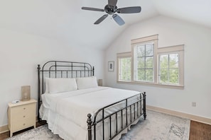 Quarto com uma cama de solteiro, mesa de cabeceira, ventilador de teto e janela com persianas.