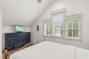 Makuuhuoneessa on sänky, lipasto, televisio ja ikkunat, joissa on sälekaihtimet.
