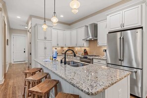 A modern kitchen with white cabinets, a stainless steel refrigerator, granite countertops, and wooden stools.
