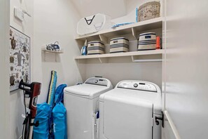Une buanderie équipée de deux machines à laver à chargement frontal, d’un étendoir et d’étagères avec des paniers et des boîtes de rangement.