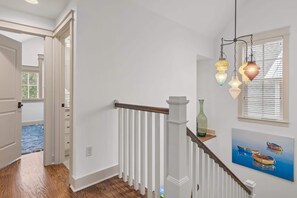 Een trap met witte leuningen, een houten handgreep en een hanglamp.