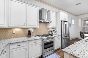 Une cuisine moderne avec des meubles blancs, une cuisinière à gaz, un réfrigérateur en acier inoxydable et un dosseret en briques.