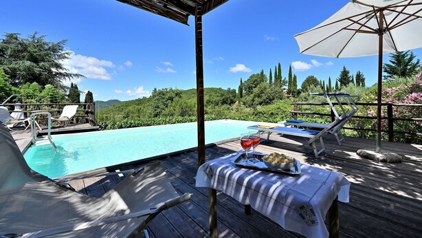 Ein Poolbereich mit Liegestühlen, einem Tisch mit Getränken und Snacks sowie Blick auf den Pool und die umliegende Bepflanzung.