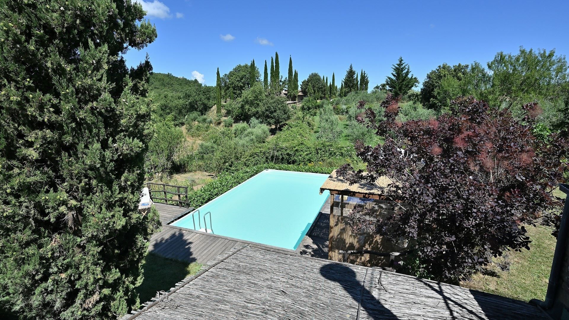 A rectangular pool with a wooden deck and a thatched roof structure nearby.