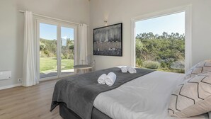 Une chambre avec un grand lit, deux fenêtres, un tableau et une vue sur la verdure.