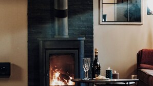 A cozy living room with a fireplace, a table with a candle, and a wine glass. - Maison Ubuntu (Beauraing)