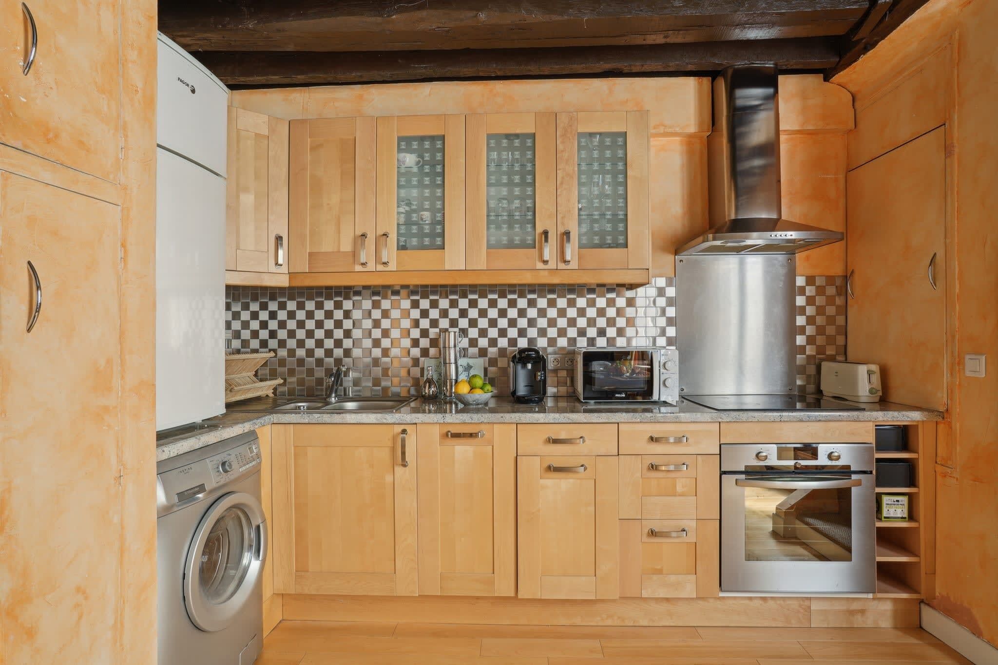 Een keuken met houten kastjes, een wasmachine, een magnetron, een broodrooster en een fornuis.