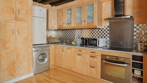 A compact kitchen with wooden cabinets, a stainless steel refrigerator, a washing machine, a microwave, and a built-in oven.