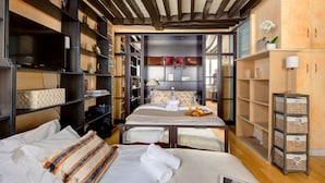 A compact hotel room with a bed, bedside tables, a desk, and built-in shelving with various items.
