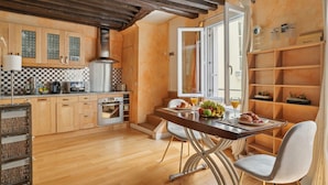 A modern kitchen with wooden cabinets, a dining area with a table and chairs, and a breakfast setup with fruits and pastries.