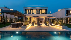 Una casa moderna con piscina, area salotto esterna e un patio ben illuminato.
