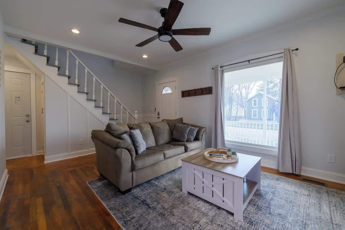 A living room with a grey sofa, a coffee table, a staircase, and a large window with curtains.