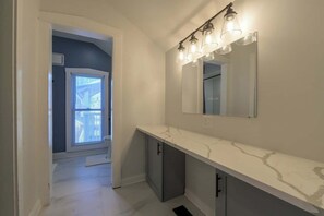 Een moderne badkamer met een witte marmeren aanrecht, een grote spiegel en een lamp boven de spiegel.