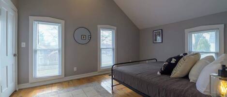 A bedroom with a sloped ceiling, two windows with blinds, a bed with a metal frame, a rug, and a ceiling fan.
