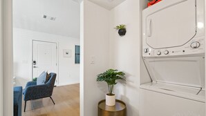 A modern living room with a blue armchair, a potted plant, and a built-in washer and dryer. - MLK #104 xxxxxxxxxxx (Austin)