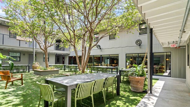 An outdoor patio area with tables and chairs, surrounded by greenery and trees. - MLK #104 xxxxxxxxxxx (Austin)