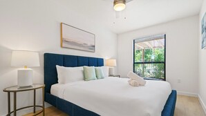 A bedroom with a large bed, two bedside tables with lamps, a window with a view of greenery, and a painting on the wall. - MLK #104 xxxxxxxxxxx (Austin)