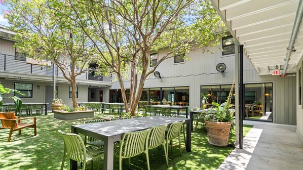 Un patio al aire libre con mesas y sillas, rodeado de follaje y árboles.