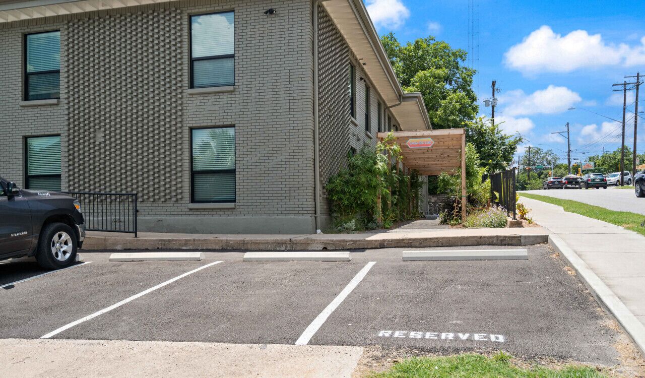A parking lot with a 'RESERVED' sign, a building with a brick facade, and a covered area with a sign.