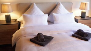 A neatly made bed with white linens, two pillows, and two folded towels on the bed. There are two bedside tables with lamps on either side of the bed. - Romantic rooftop apartment (Windach)