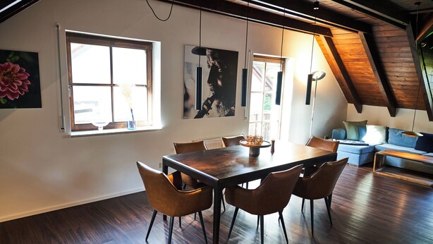 A dining area with a wooden table and chairs, large windows, and a loft-style ceiling. - Romantic rooftop apartment (Windach)