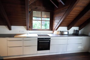 A modern kitchen with a built-in dishwasher, a window with blinds, and a countertop with a kettle and toaster. - Romantic Penthouse Apartment (Windach)