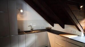 A modern kitchen with white cabinetry, a black countertop, and a wooden ceiling. - Romantic rooftop apartment (Windach)