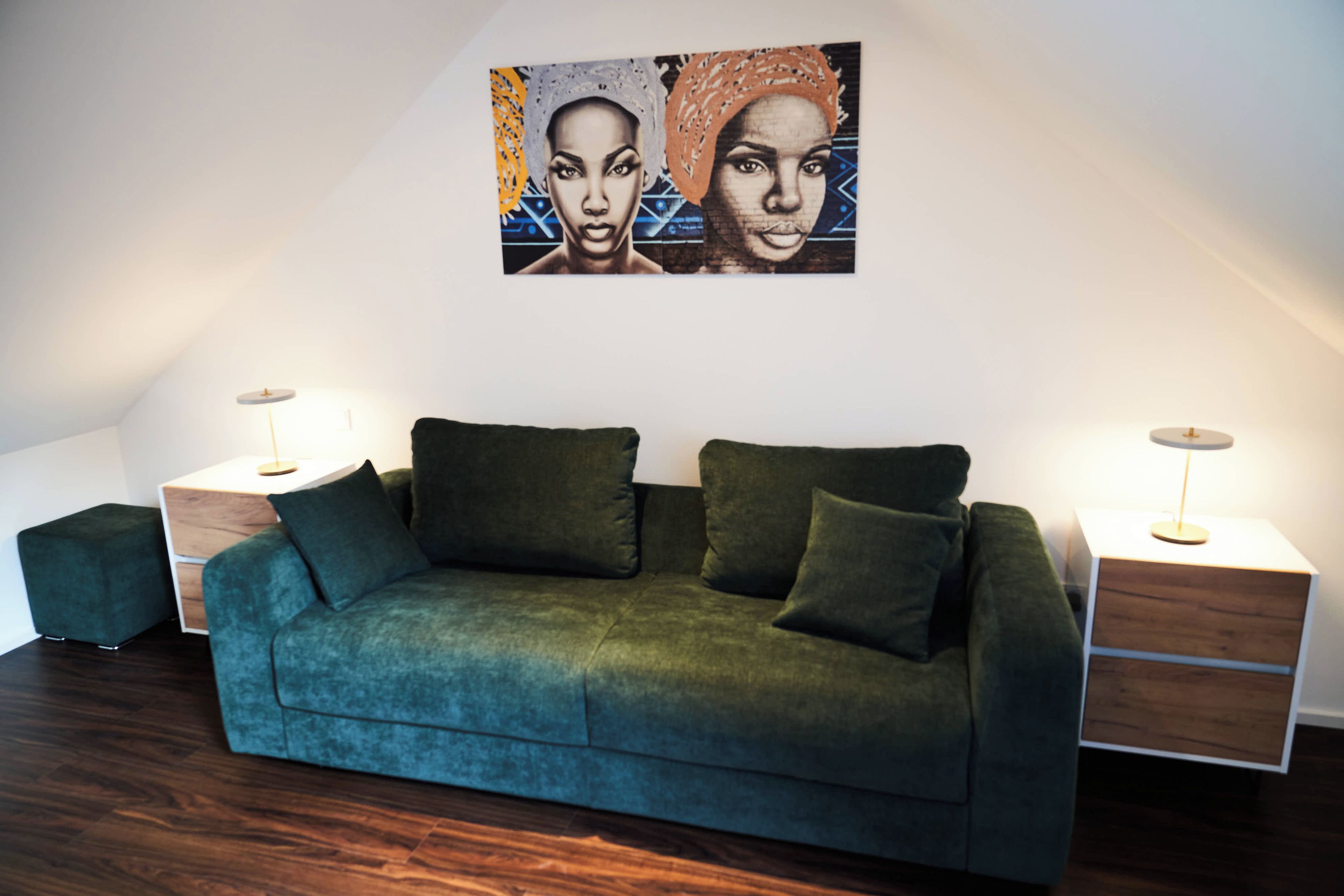 A modern living room with a teal sofa, two side tables, and a wall-mounted artwork.