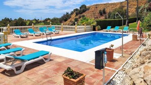 Une piscine rectangulaire à l’eau bleue, entourée d’une terrasse carrelée avec des chaises longues blanches et bleues.