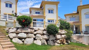 Un immeuble à plusieurs étages, doté d’une façade jaune, de balcons blancs et d’un mur de soutènement en pierre agrémenté de verdure.