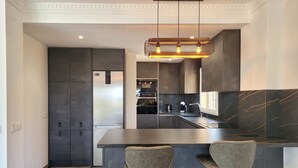 Une cuisine moderne avec des meubles de couleur sombre, un pare-feu en marbre et un îlot central doté de tabourets de bar.