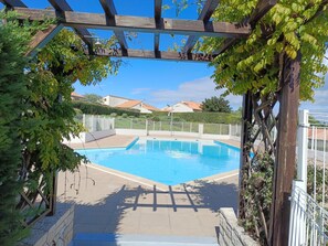 En swimmingpool med en pergola ovanför, omgiven av grönska och ett staket.