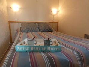 Un lit avec une literie à rayures, deux oreillers et un plateau avec des tasses et une pancarte indiquant « Notre-Dame-des-Monts ».