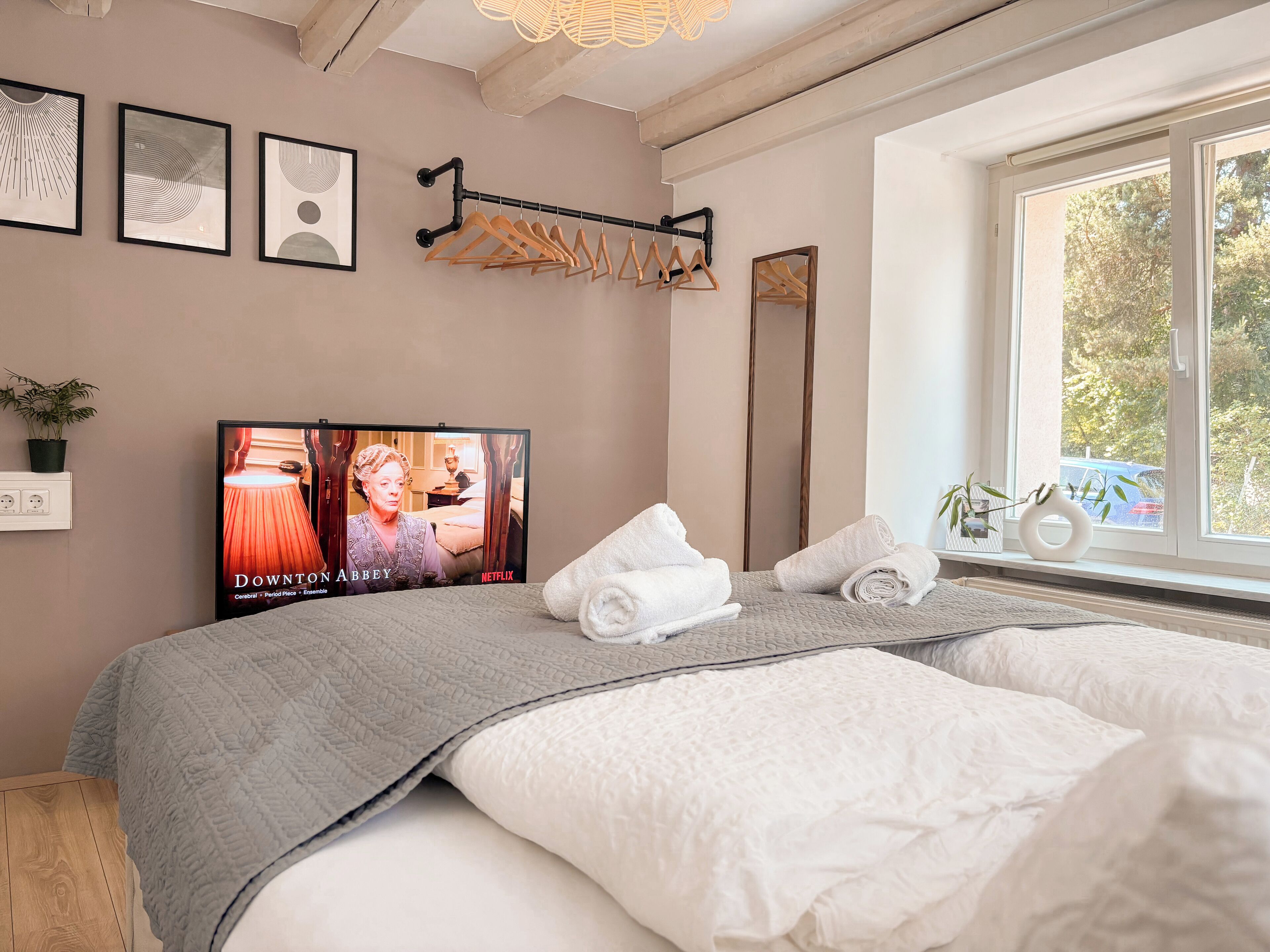 Une chambre d’hôtel avec un grand lit, un téléviseur fixé au mur, une fenêtre donnant sur la verdure et un porte-manteau en bois.