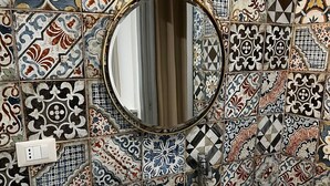 A bathroom with a tiled wall, a round mirror, a sink with a stone basin, and a towel on the counter. - Masseria Torre Saracena (Favara)