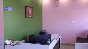 A reception area with a green wall, a Buddha statue, a clock, and a reception desk with chairs and a computer. - Hotel Roop Shree Inn By GRB (Patna)