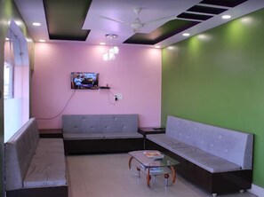Un área de espera moderna con un sofá gris, una mesa de vidrio y un televisor montado en la pared.