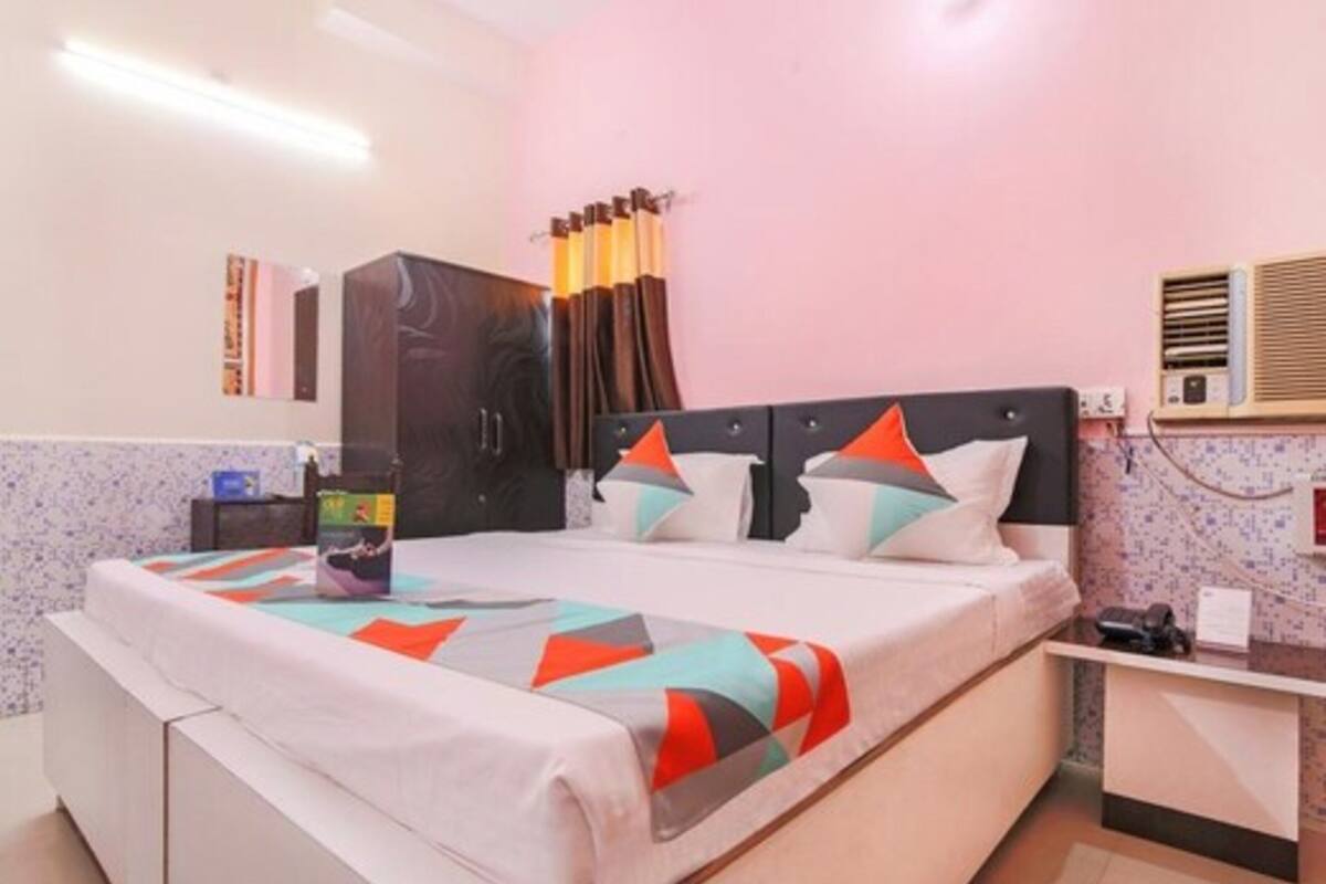 A hotel room with a bed, a desk, a wardrobe, and an air conditioning unit.