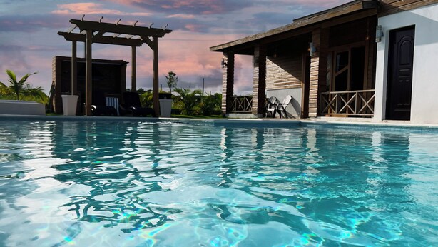 A clear swimming pool with a wooden pergola and lounge chairs, surrounded by a building with a wooden facade and a black door.