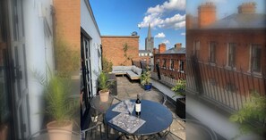 Une cour avec une table ronde, des plantes en pot et un bâtiment en briques en arrière-plan.