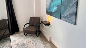 Une pièce avec un tapis à motifs, une chaise, une étagère fixée au mur avec une lampe, et une grande œuvre d’art sur le thème de l’océan.