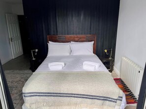 Ein ordentlich bezogenes Bett mit weißen Leinen und Decke, ein hölzerner Kopfteil, ein Nachttisch mit Lampe und eine Heizung.