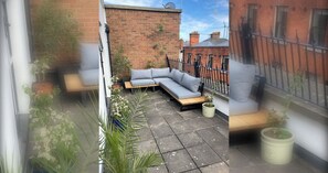 A patio with a grey sofa, potted plants, and a brick wall.