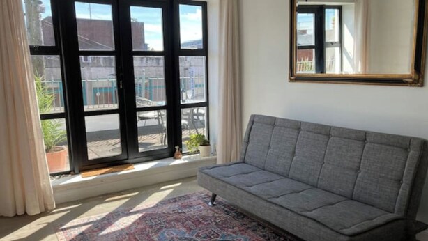 A room with a grey sofa, a patterned rug, a large window with a view of buildings, and a mirror on the wall. - 2 Bed City Centre Penthouse with Cathedral Views (Dublin)
