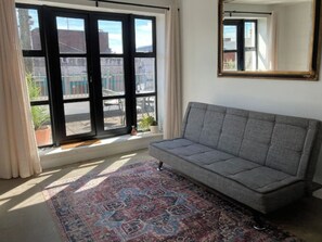A room with a grey sofa, a patterned rug, a large window with a view of buildings, and a mirror on the wall. - 2 Bed City Centre Penthouse with Cathedral Views (Dublin)